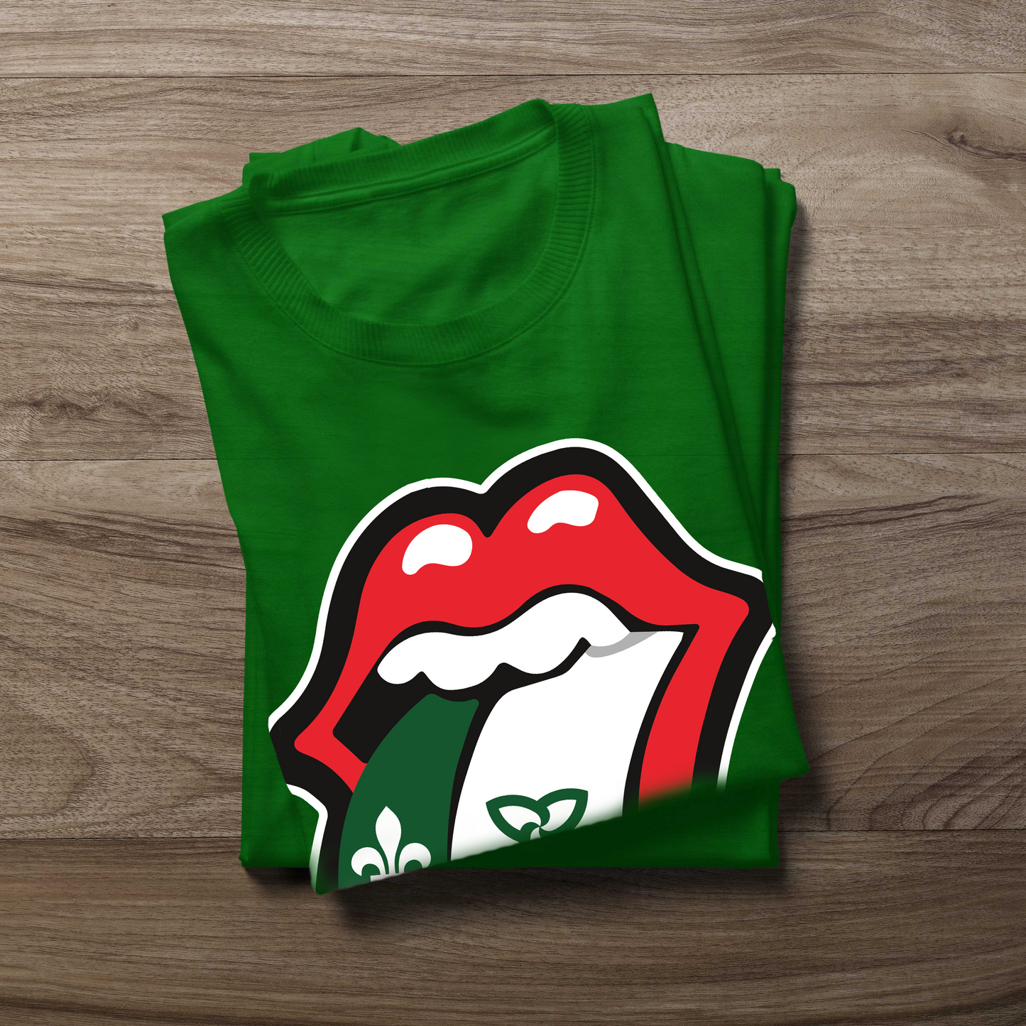 A folded green t-shirt with a graphic of red lips with white teeth and black outlines, revealing a green and white franco ontarien tongue , placed on a brown wood-grain surface.