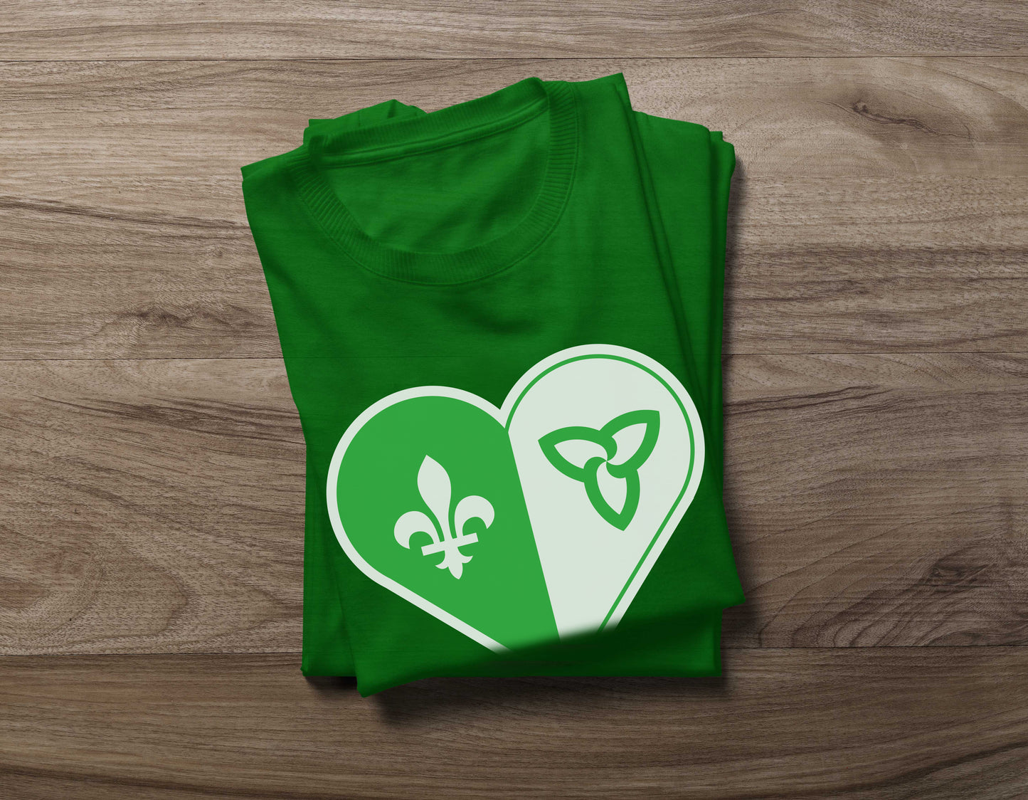 Folded Green Franco-Ontarian Heart Flag Shirt on a wooden background, featuring a design of the Franco flag in the shape of a heart.