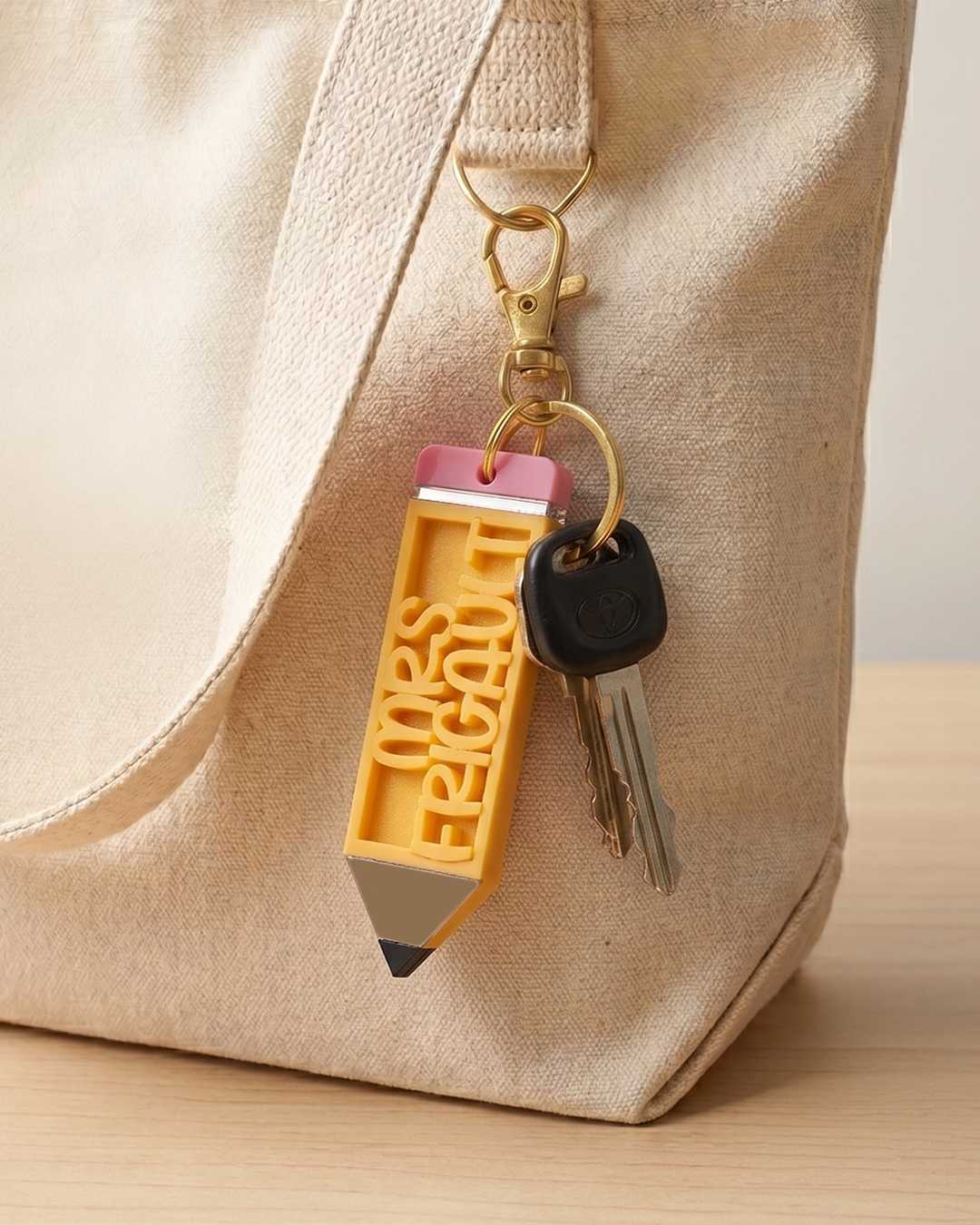 Keychain shaped like a pencil customized with teacher name attached to a beige bag.