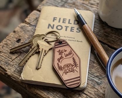 Field Notes notebook with keys and a leather let's get lost keychain on a wooden surface.