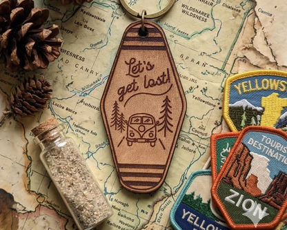 Leather keychain with 'Let's get lost' design on a map background with patches and bottle.