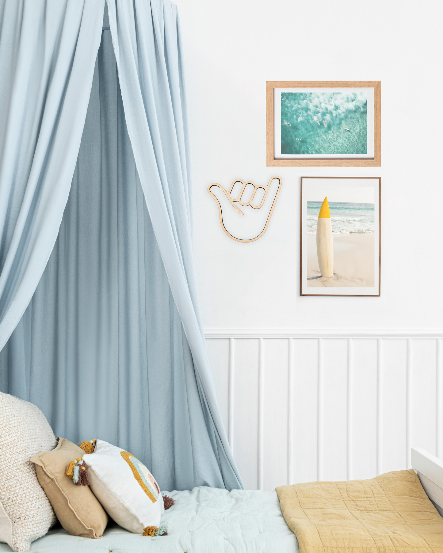 bedroom with a blue canope bed and beach themed artwork on the wall including a photo of a surf board, waves and a wooden cutout of the shaka hand sign