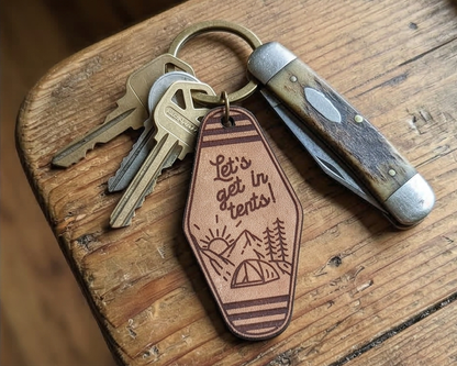 Keychain with engraved Let's get in tents design and text on a wooden surface