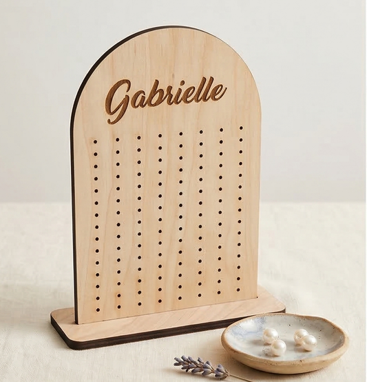 Wooden jewelry holder with 'Gabrielle' engraved, next to a small dish with earrings on a light background