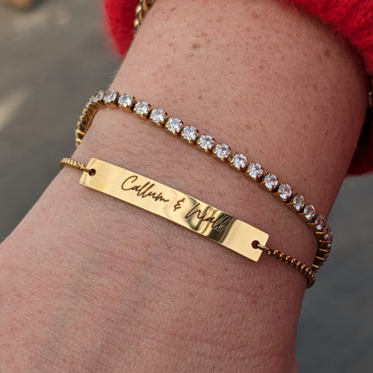 Gold bracelet with engraved name on wrist against a blurred background