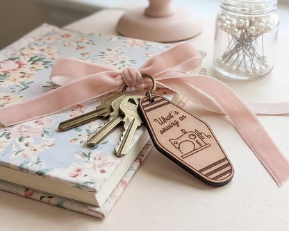 Keys with a leather what`s sewing on keychain on a floral notebook with a pink ribbon.