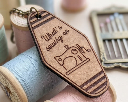 Leather keychain with sewing-themed design and text, placed on spools of thread.
