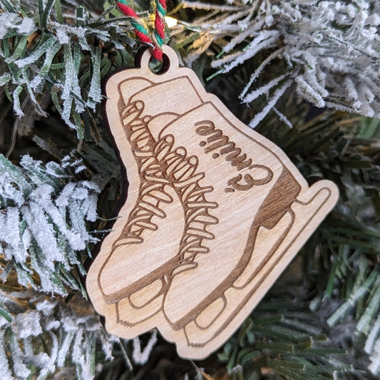 A custom wooden figure skate ornament with a 'Emilie' inscription, hanging on a Christmas tree with a red ribbon.