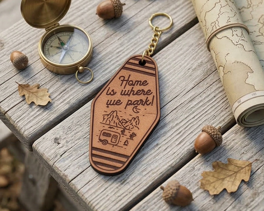 Leather keychain with 'Home is where you park' text and compass on wooden surface with acorns and map.
