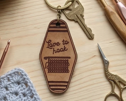 Brown leather keychain with 'Love to hook' text on a wooden surface with crochet and scissors.