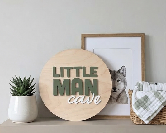 Decorative sign with 'Little Man Cave' text, framed picture of a wolf, and plant on a shelf.