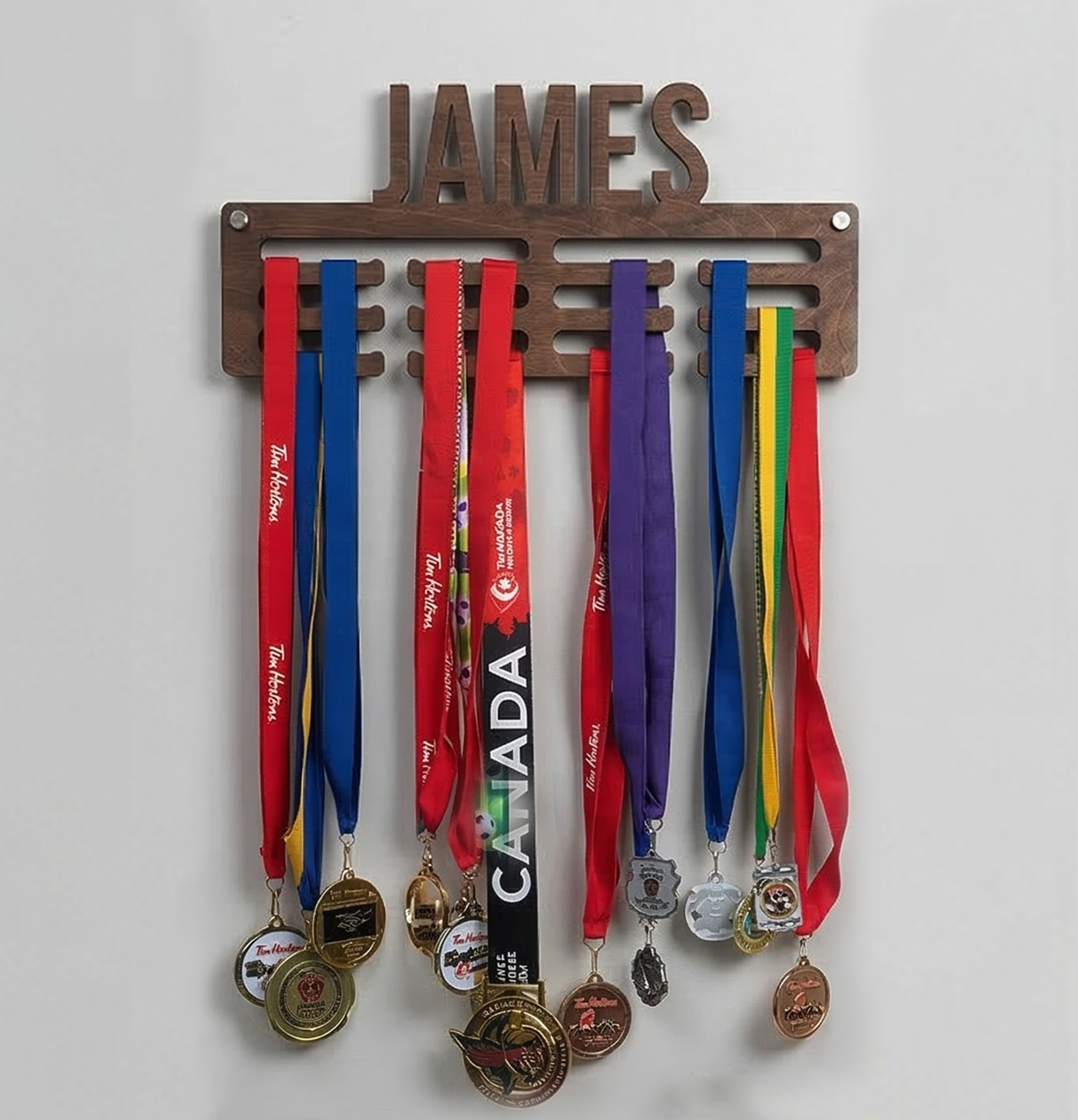 Medal holder with medals and ribbons hanging on a white wall, personalized with 'JAMES'.