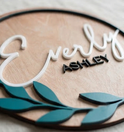 Wooden plaque with 'Everly Ashley' text and teal leaf designs.