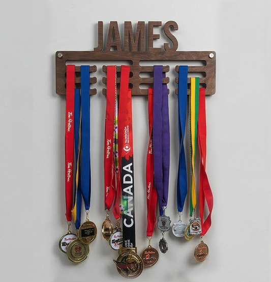 Medal holder with medals and ribbons hanging on a white wall, personalized with 'JAMES'.