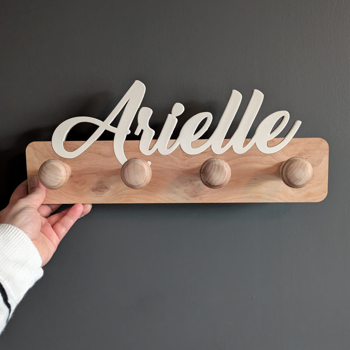 Personalized wooden towel rack with the name "Arielle" in white script on a natural wood base with four rounded pegs, handmade from layered plywood.