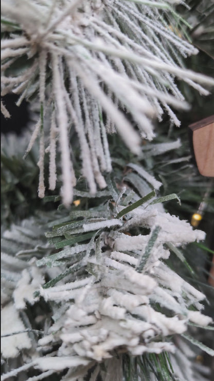 camera paning on a snowey artifical chrismtas tree showing a wooden christmas ornament in the shape of a onesie engraved with coming soon