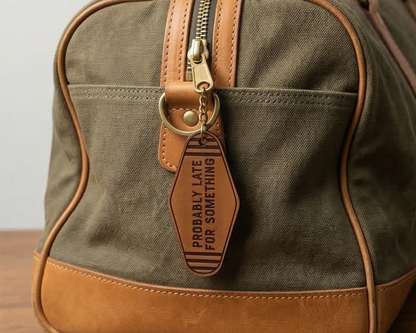 Green bag with brown leather accents and a keychain that says probably late for something on a light background