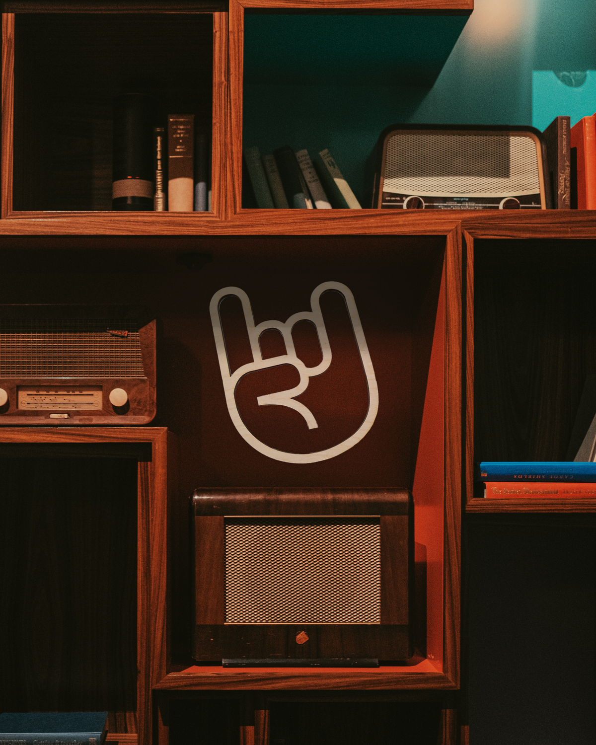 A wooden cutout of a 'Rock On' hand sign displayed on a shelf with various items in the background, including books and a vintage radio.