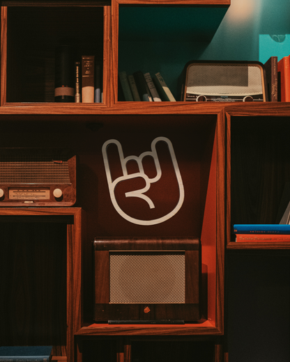A wooden cutout of a 'Rock On' hand sign displayed on a shelf with various items in the background, including books and a vintage radio.