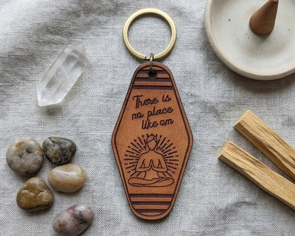 Leather keychain with engraved text There is no place like om and  a yoga pose design on a textured surface with stones 