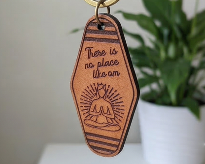 Brown leather keychain with yoga illustration and text on a white surface with a plant in the background
